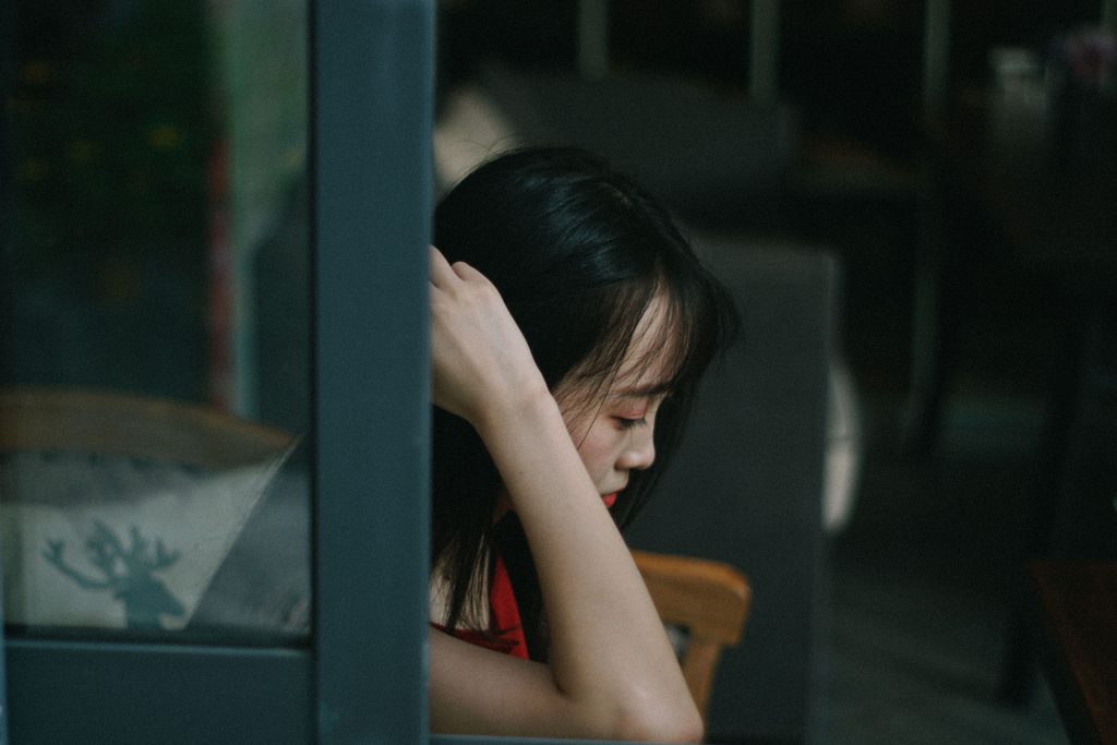 A young Asian woman looks down towards the floor in a moody shot. Thinking about how she might be strong enough to stop sinning. A young Asian woman looks down towards the floor in a moody shot. Thinking about how she might be strong enough to stop sinning.
