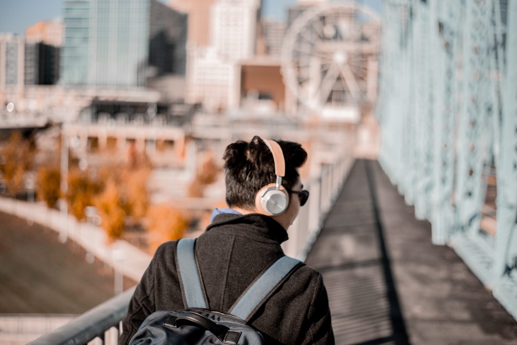 An Asian man walks across a bridge in a large city, with headphones on and listening to a podcast. An Asian man walks across a bridge in a large city, with headphones on and listening to a podcast.